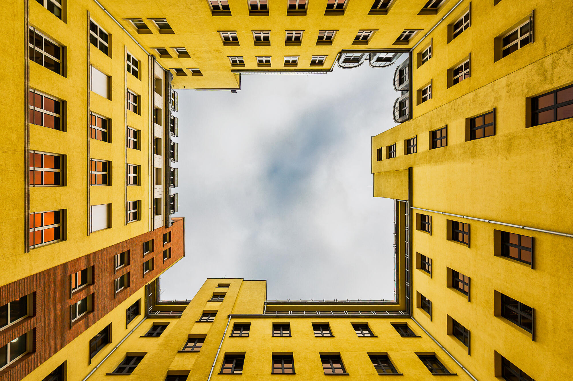 Blick aus einem Innenhof im Quartier Schützenstraße nach oben: Gelbe Fassaden rahmen den bewölkten Himmel.