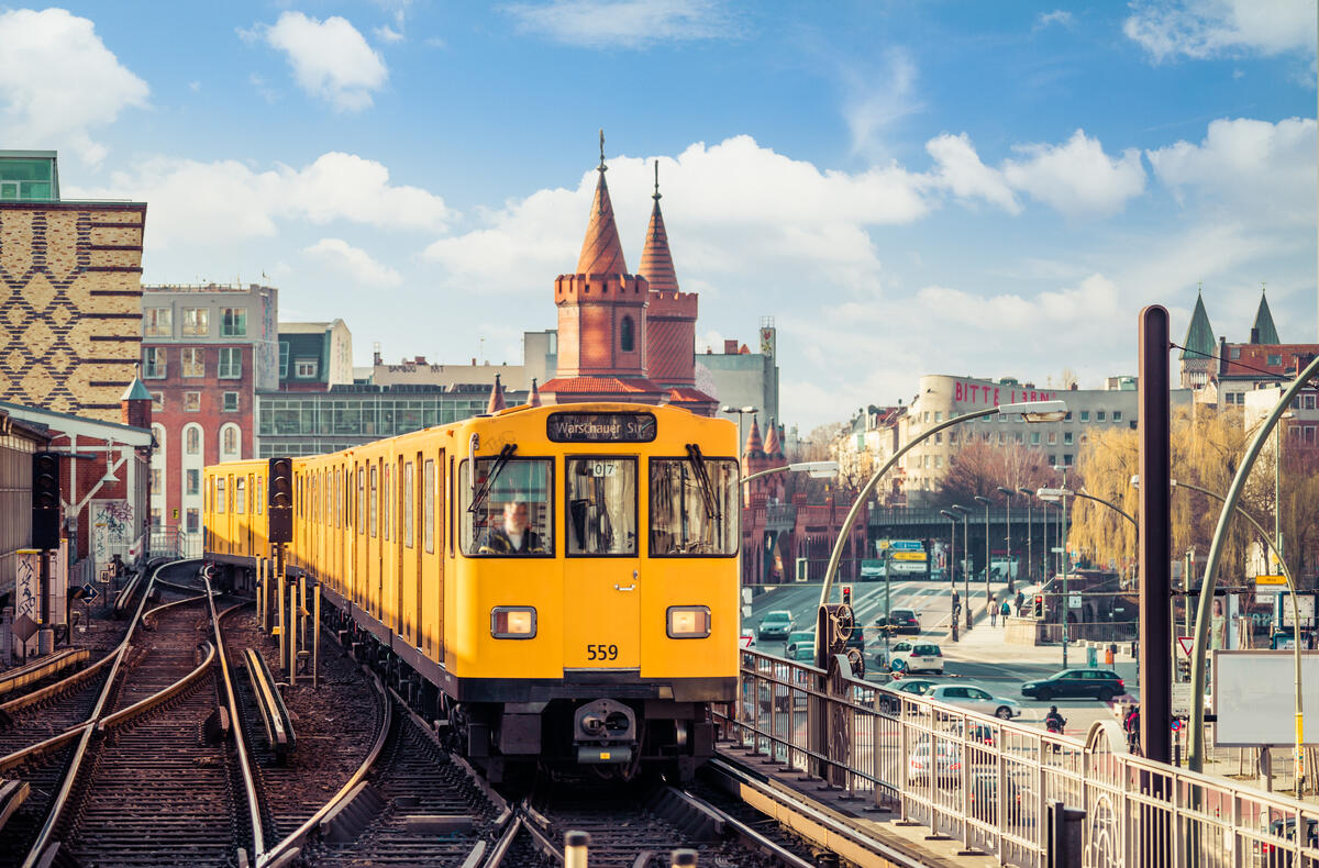 Eine gelbe U-Bahn fährt vor den roten Türmen der Oberbaumbrücke; darüber stehen helle Wolken.