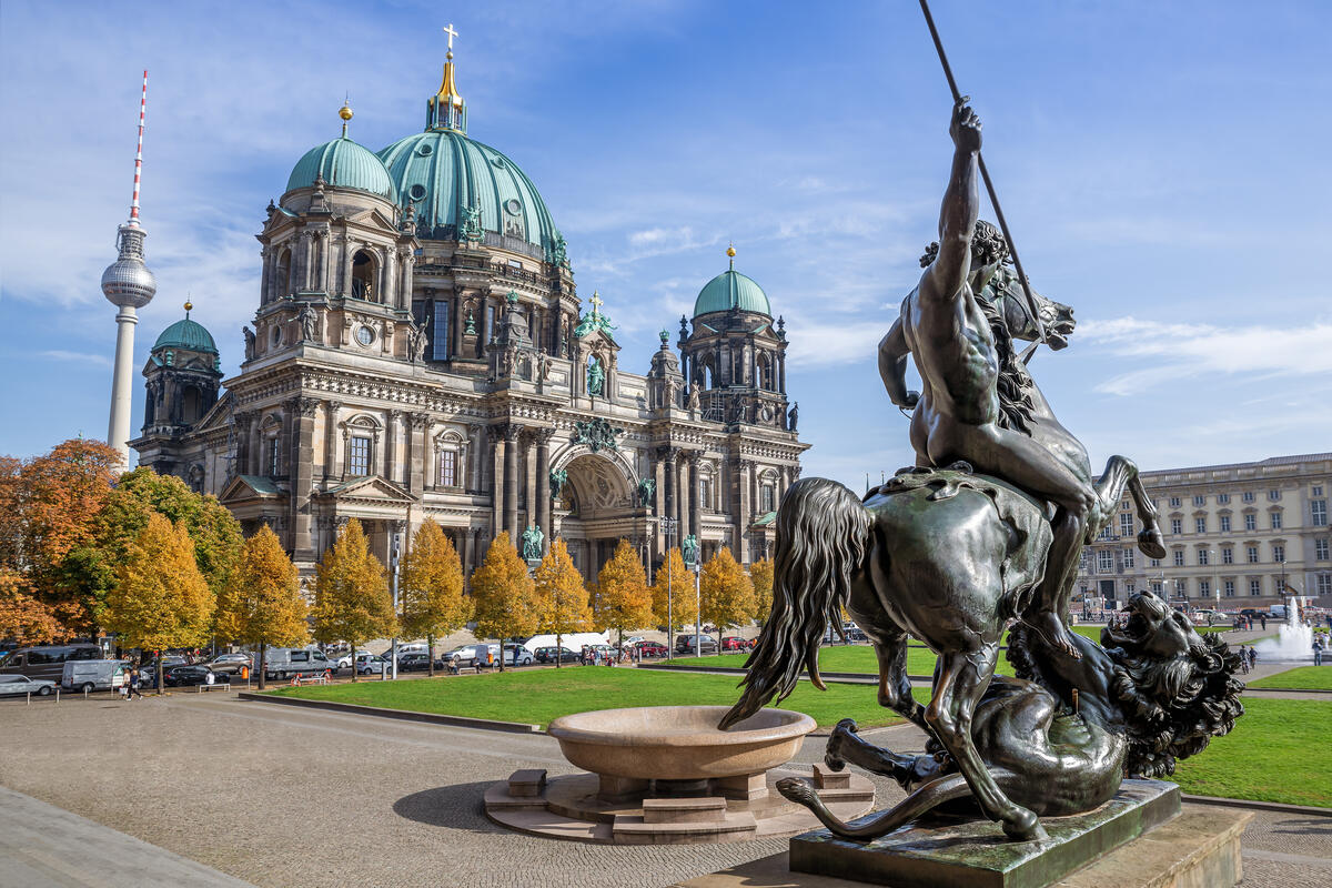 Berliner Dom und Fernsehturm hinter einem bronzenen Reiterstandbild und herbstlich gefärbten Bäumen.