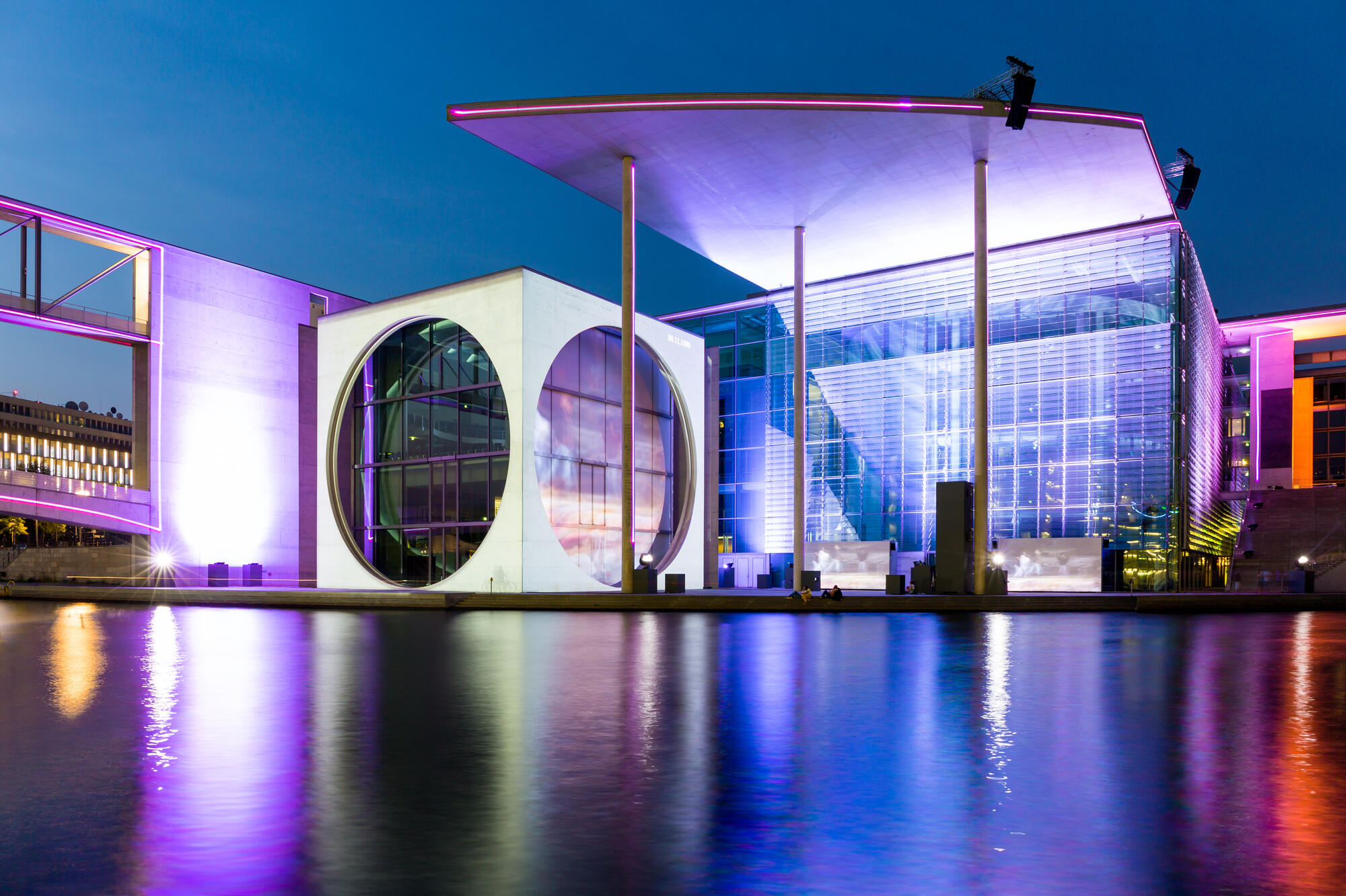 Das Marie-Elisabeth-Lüders-Haus an der Spree mit blau und violett beleuchteter Glasfassade und großem Rundfenster.