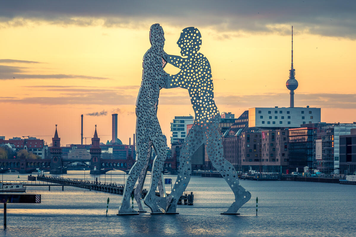 Die Skulptur Molecule Man in der Spree vor einem goldenen Himmel; dahinter Oberbaumbrücke und Fernsehturm.