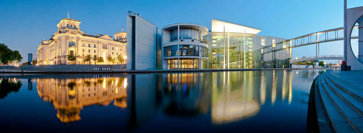 Reichstag und Paul-Löbe-Haus am Spreeufer mit beleuchteten Fassaden und Spiegelungen in der blauen Stunde.