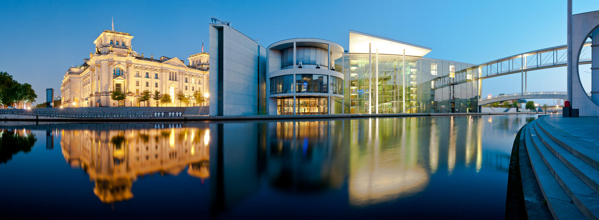 Reichstag und Paul-Löbe-Haus am Spreeufer mit beleuchteten Fassaden und Spiegelungen in der blauen Stunde.