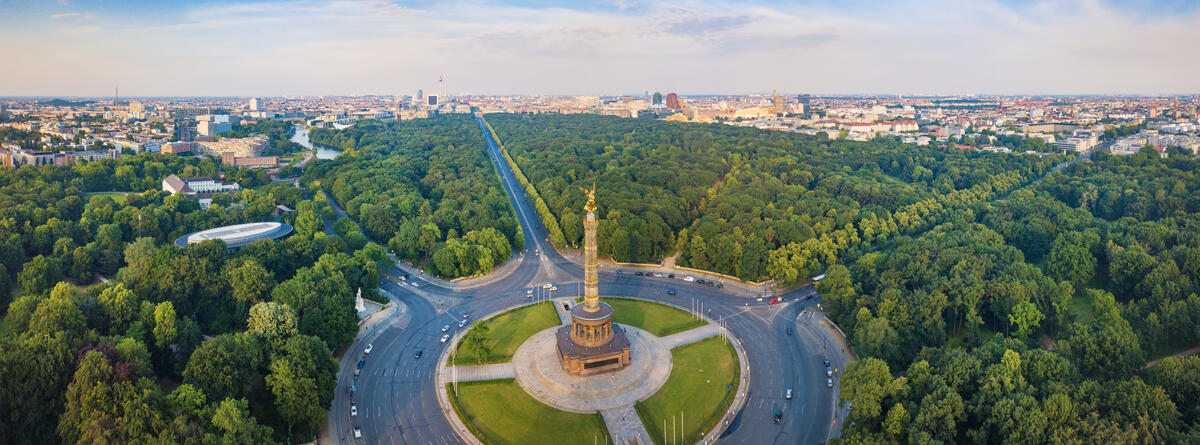 Die Siegessäule am Großen Stern zwischen den Baumkronen des Tiergartens; dahinter die Berliner Innenstadt.