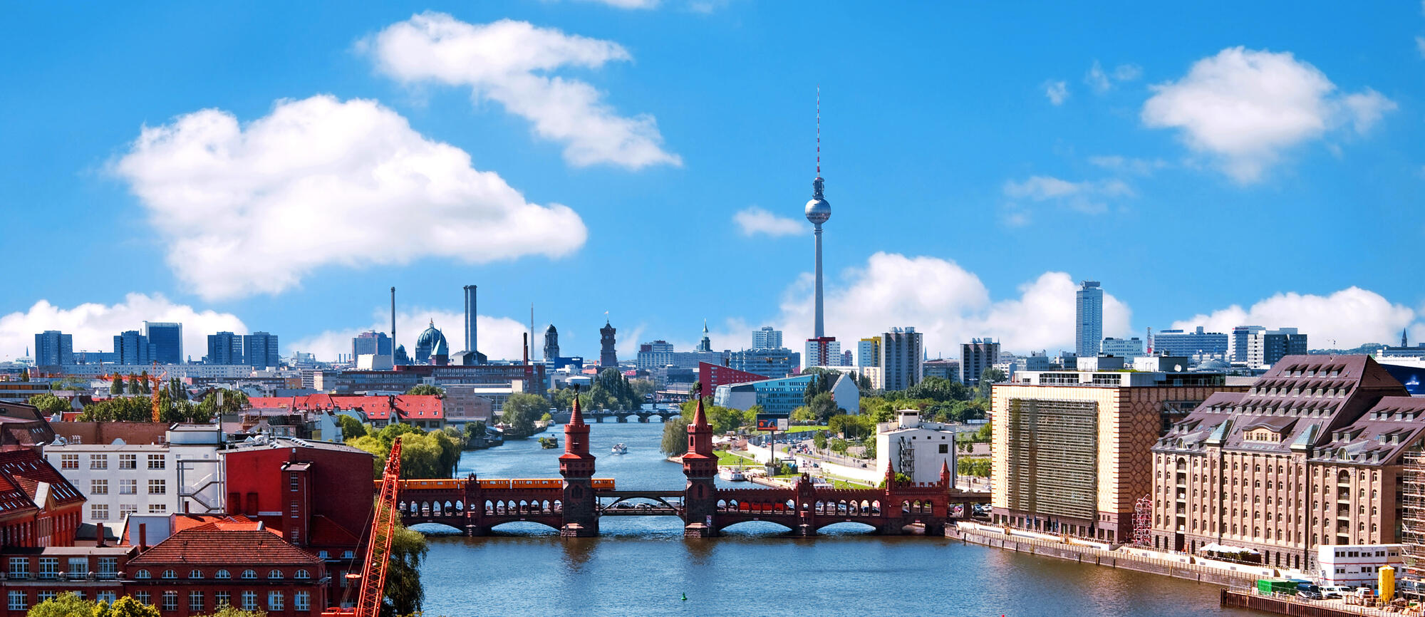 Blick über die Spree auf die Oberbaumbrücke mit gelber U-Bahn und weißen Quellwolken.