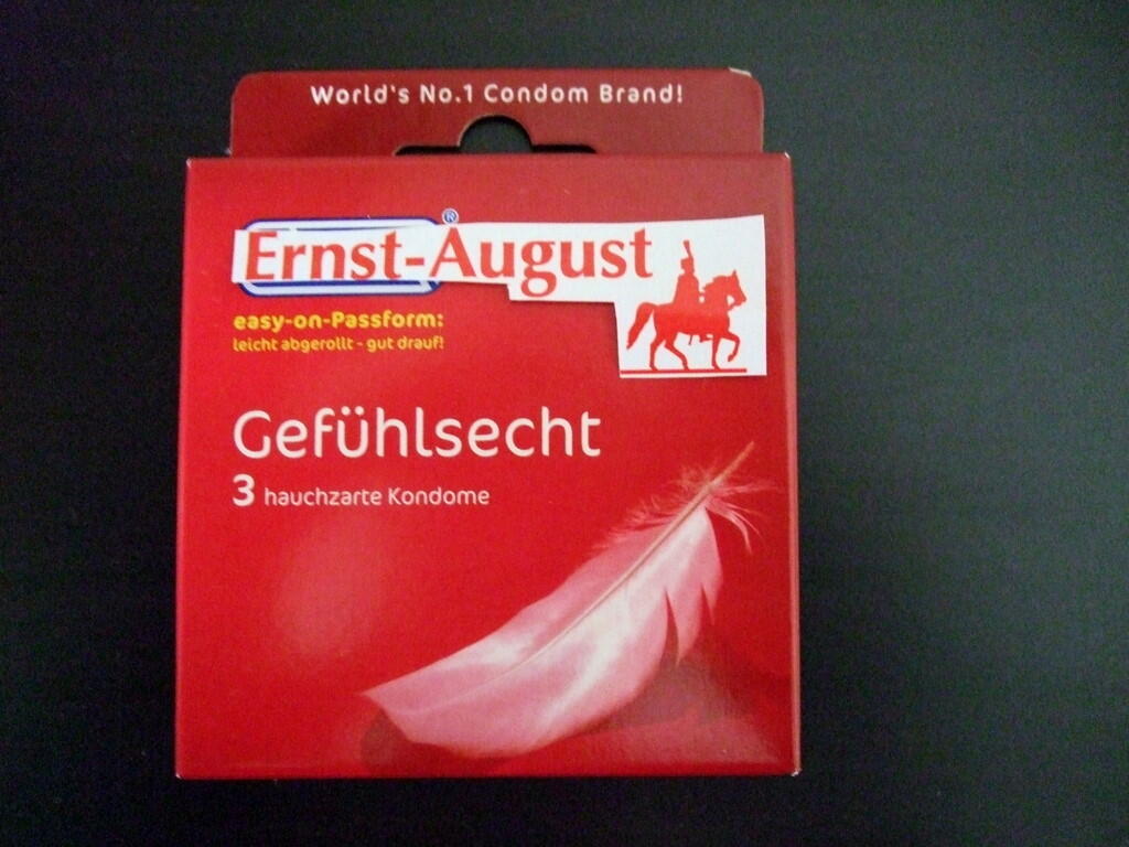Rote Packung mit Aufdruck zu hauchzarten Kondomen und weißer Feder vor dunklem Hintergrund.