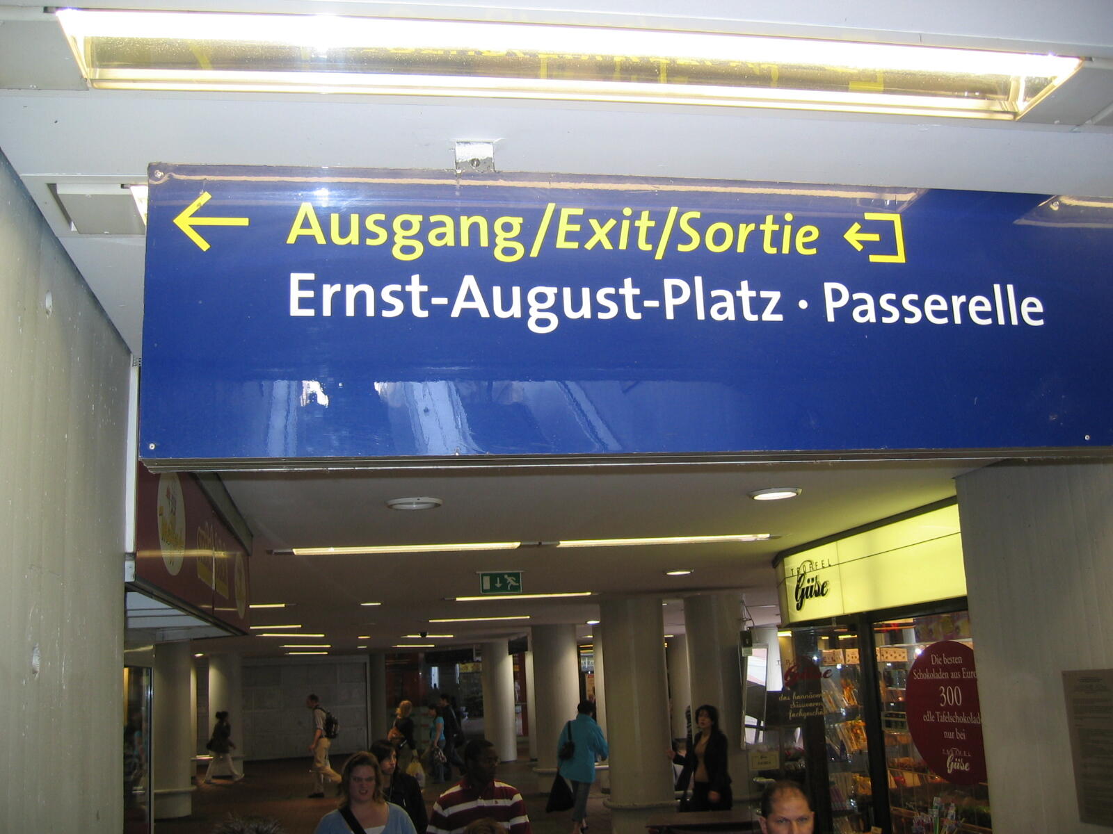 Blaues Ausgangsschild über einer belebten Bahnhofspassage mit Hinweisen zum Ernst-August-Platz.
