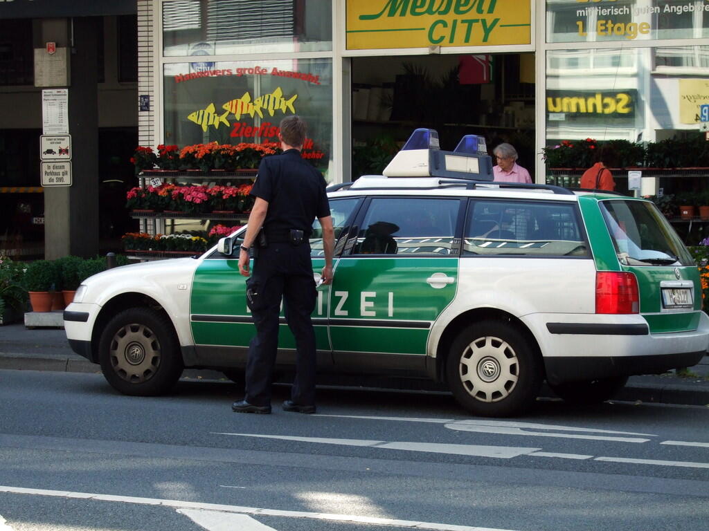 Grün-weißer Polizeiwagen mit Polizist vor einem Blumengeschäft