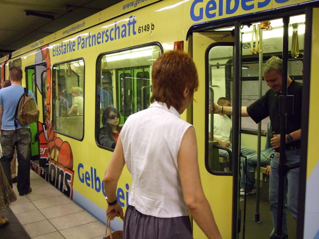 Mehrere Personen stehen an der offenen Tür eines gelben U-Bahn-Wagens in einer Station.