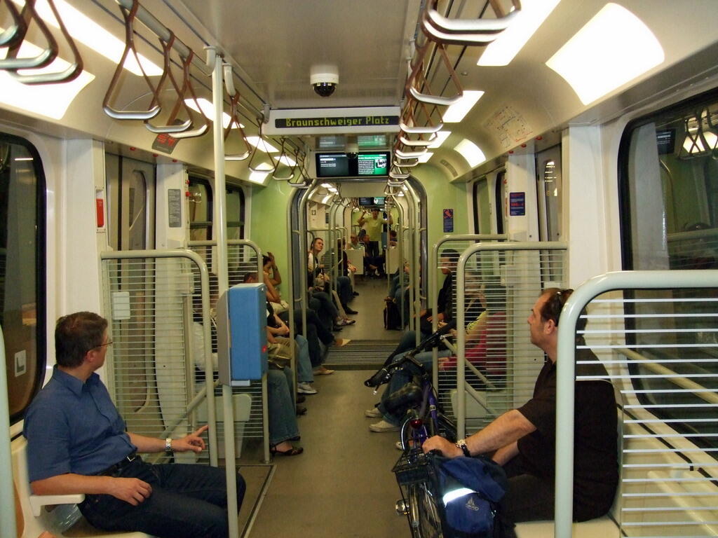 Blick durch einen U-Bahn-Wagen mit sitzenden Fahrgästen, Haltestangen und einem Fahrrad im Vordergrund.
