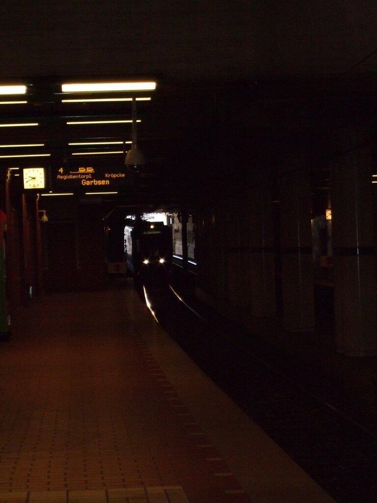 U-Bahn-Zug mit eingeschalteten Scheinwerfern an einem dunklen, beleuchteten Bahnsteig.