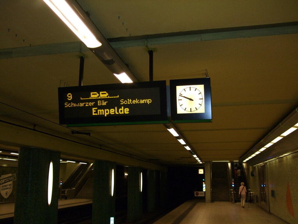 Leerer U-Bahn-Bahnsteig mit Stationsschild Empelde, Uhr, Beleuchtung und einer Person im Hintergrund.