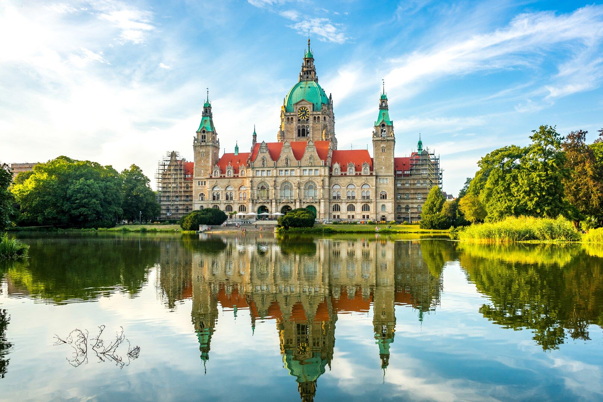 Neues Rathaus Hannover mit Kuppel und Türmen, gespiegelt im Maschteich bei Sonne und lockeren Wolken.