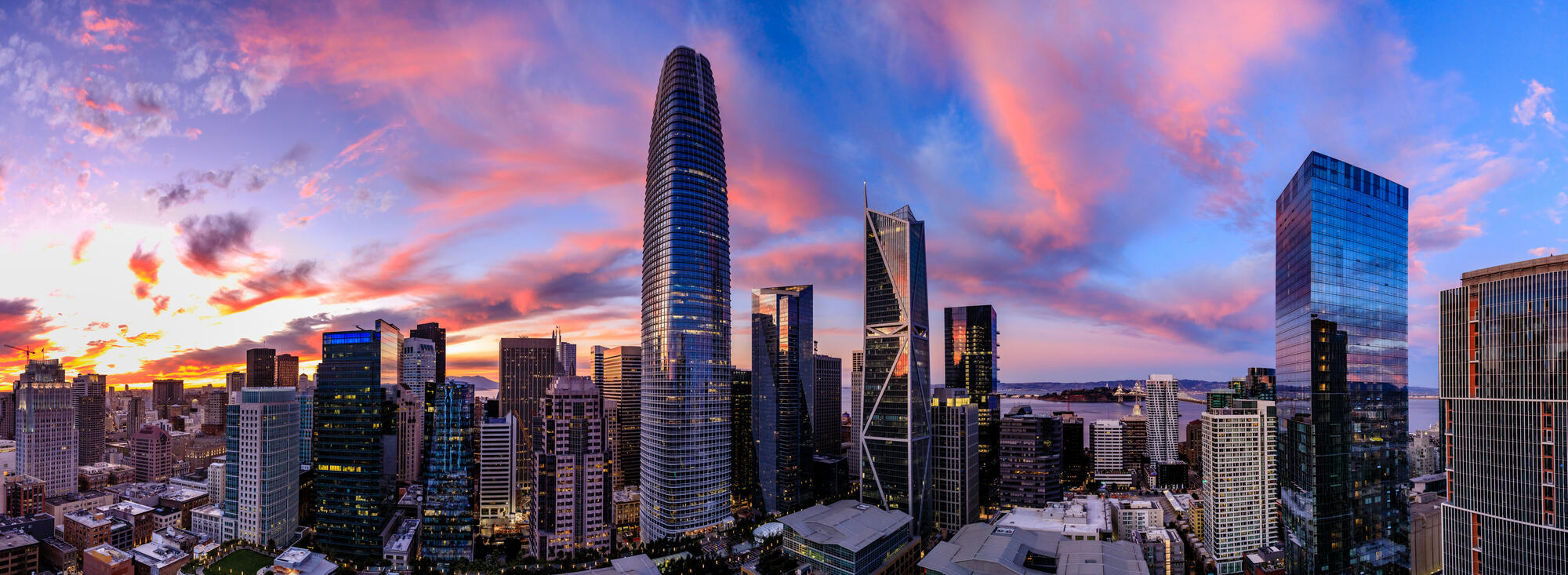 Der abgerundete Salesforce Tower ragt aus der Innenstadt unter einem rosa und blau gefärbten Abendhimmel hervor.