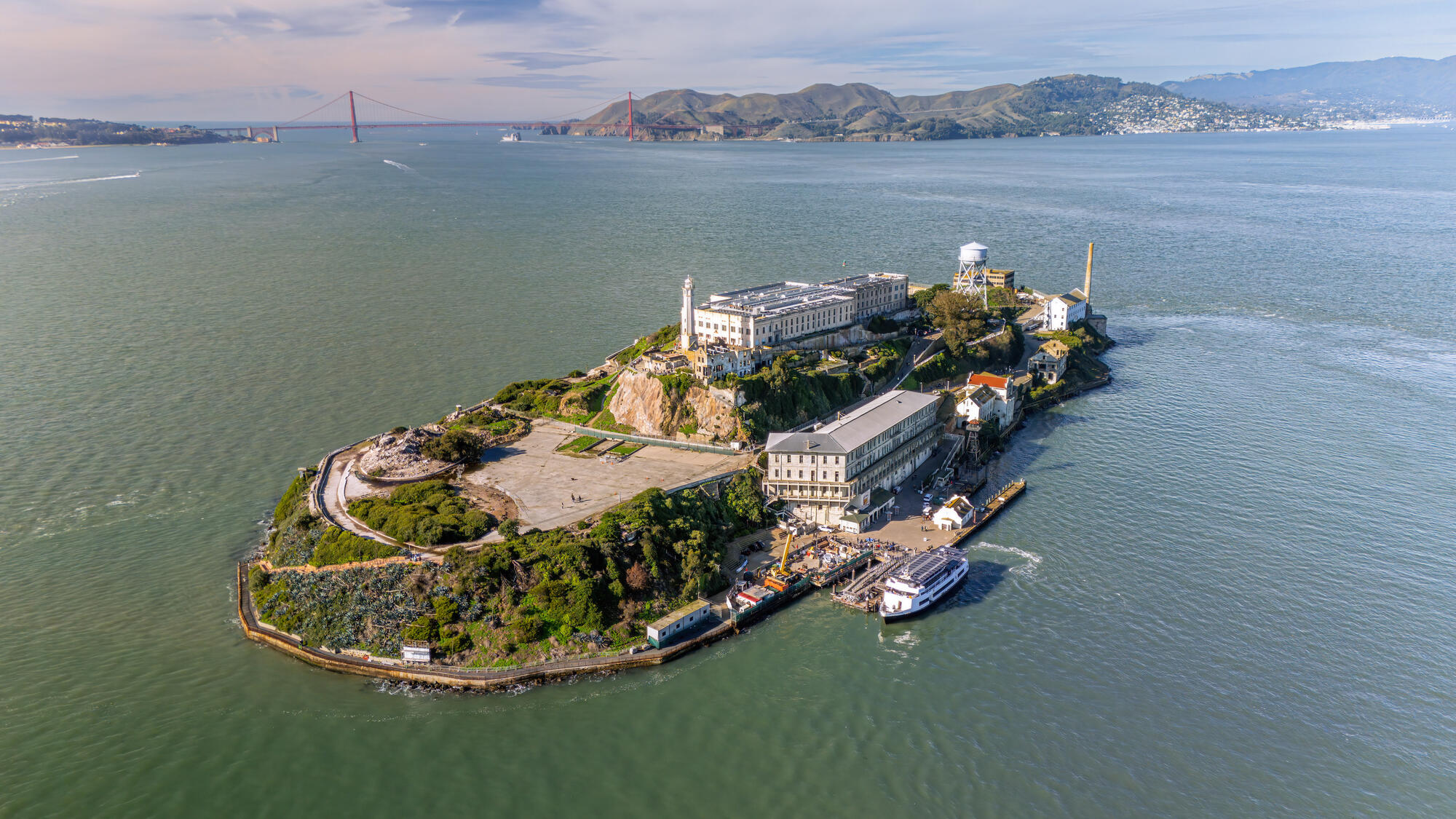 Die Insel mit Gefängnisgebäuden, Wegen und Anlegestelle liegt in der Bucht; am Horizont ist die Golden Gate Bridge zu erkennen.