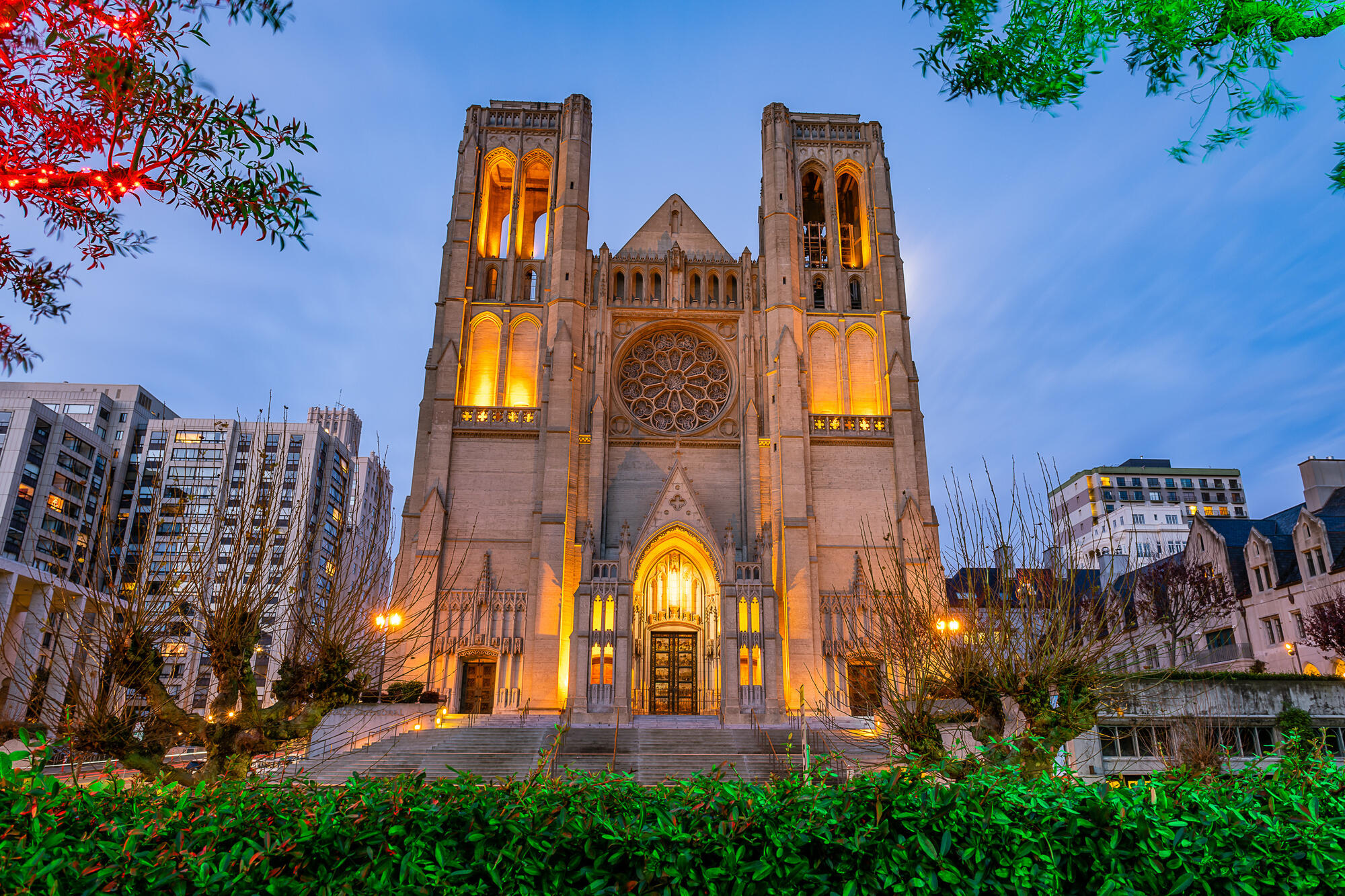 Warmes Licht betont die Glockenfenster, die Rosette und den Eingang der Grace Cathedral in der Abenddämmerung.