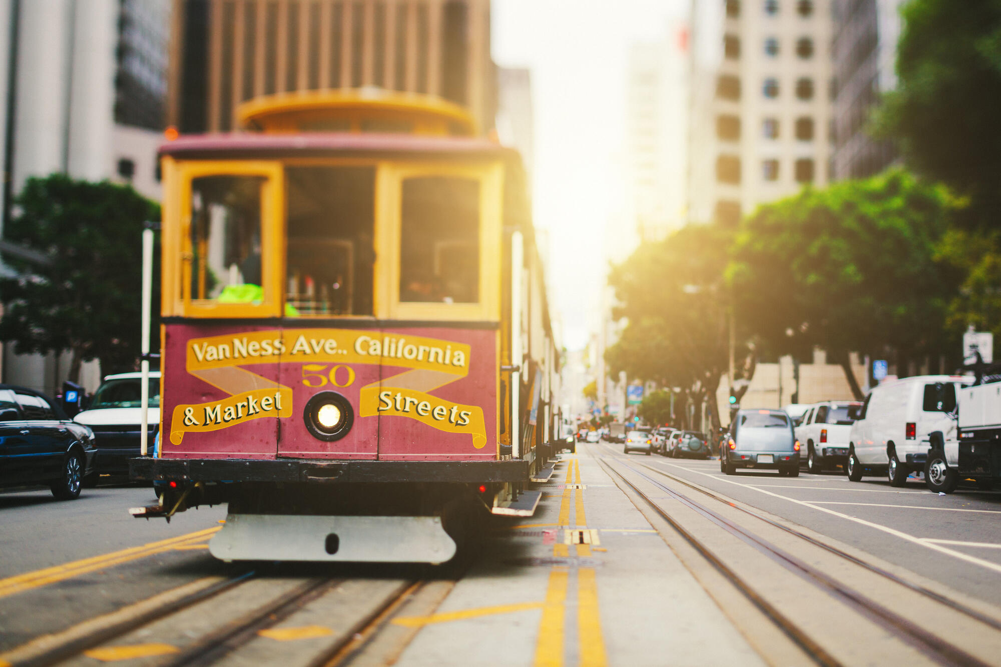 Ein rot-gelbes Cable Car fährt zwischen hohen Gebäuden durch das warme Licht der California Street.