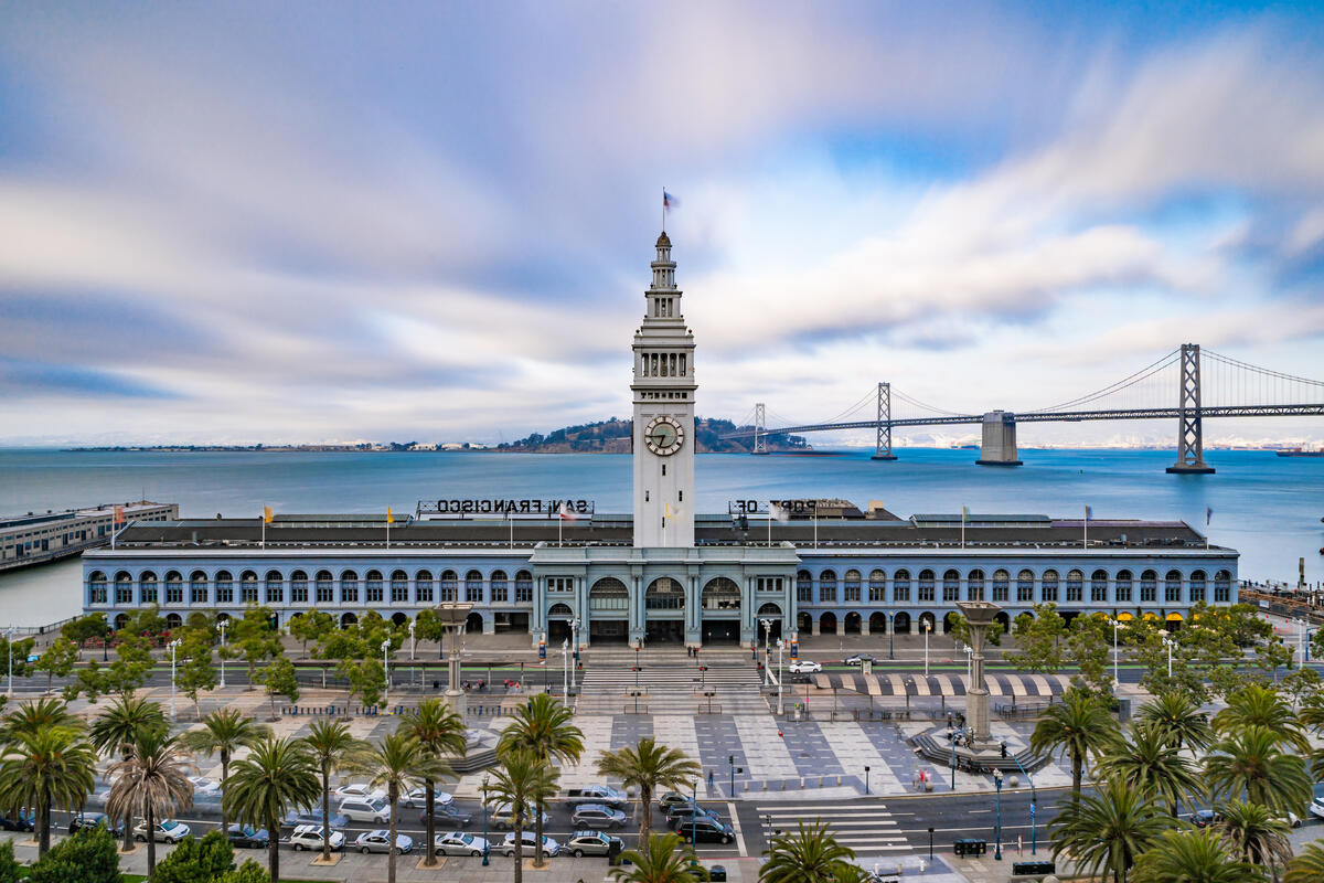 Der Uhrturm des Ferry Building steht über der langen Arkadenfront; hinter dem Gebäude verläuft die Bay Bridge.