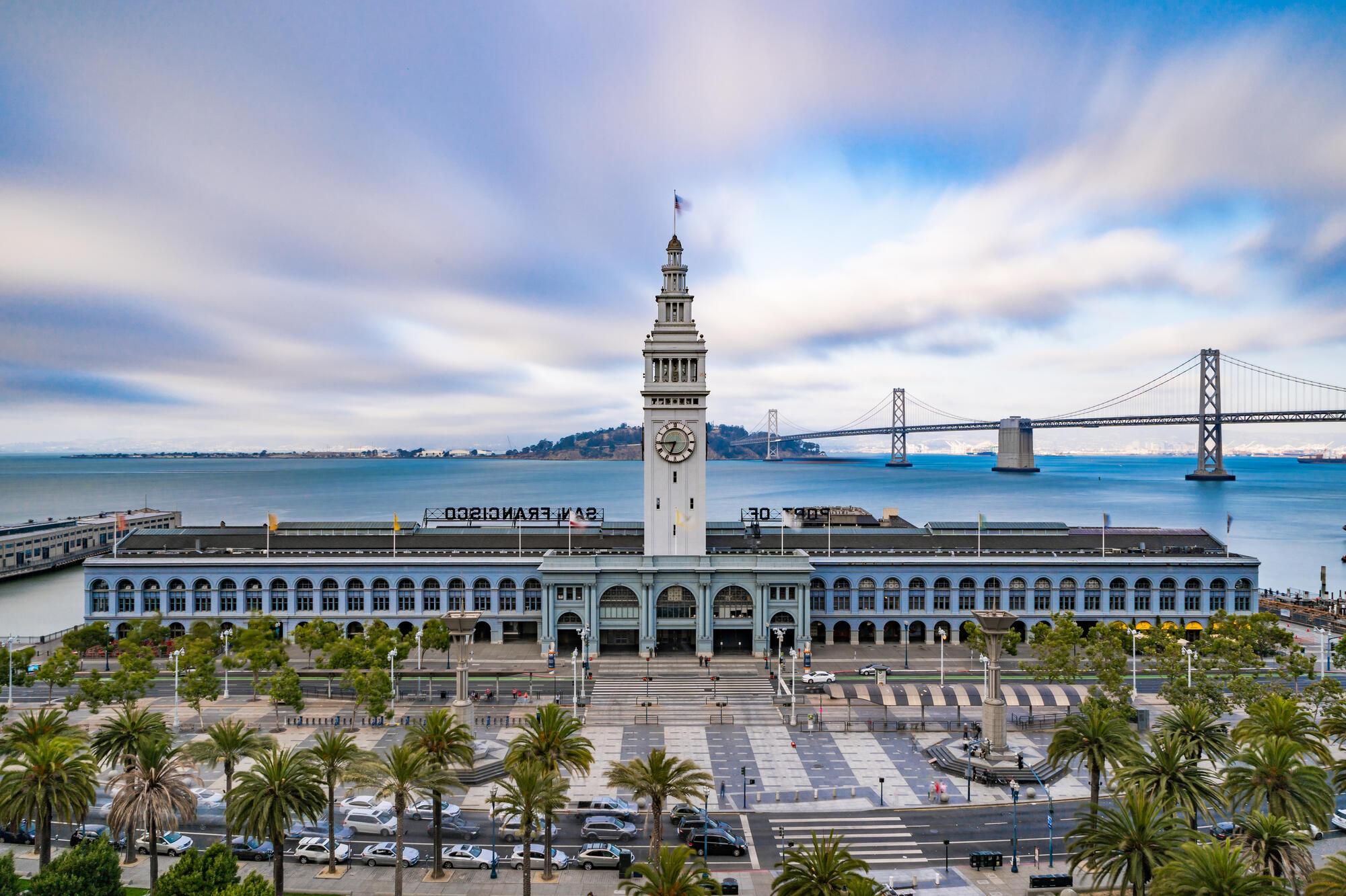 Der Uhrturm des Ferry Building steht über der langen Arkadenfront; hinter dem Gebäude verläuft die Bay Bridge.