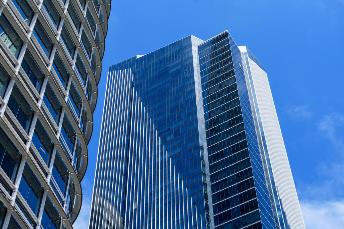 Blick nach oben auf blaue Glasflächen, helle vertikale Fassadenstreifen und den gebogenen Rand des Salesforce Tower.