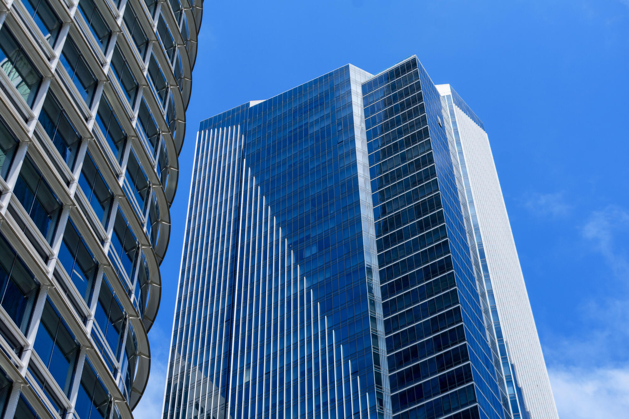 Blick nach oben auf blaue Glasflächen, helle vertikale Fassadenstreifen und den gebogenen Rand des Salesforce Tower.