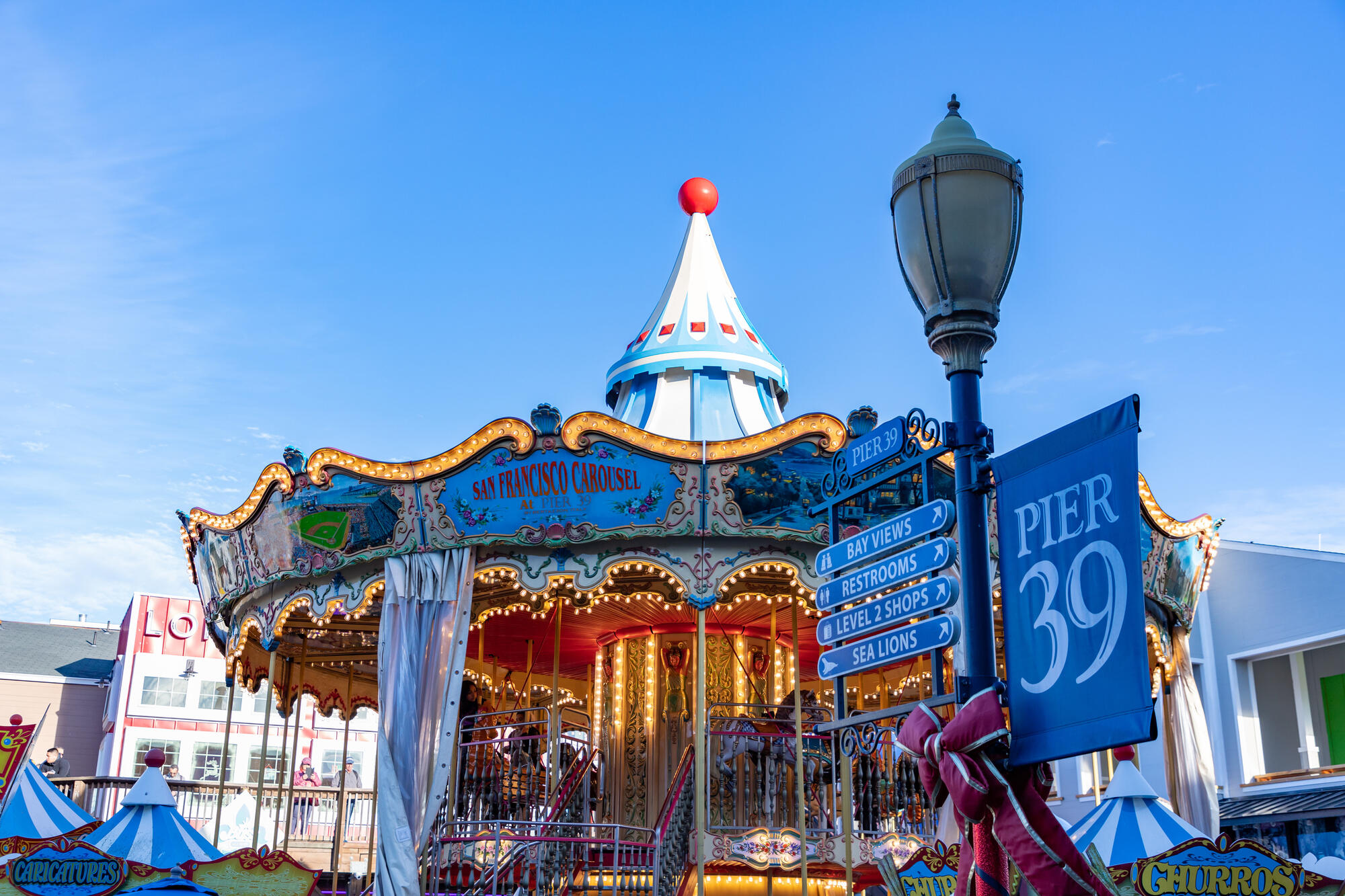 Das blau-weiße Dach und die goldfarbenen Verzierungen des Karussells stehen neben den Wegweisern von Pier 39.