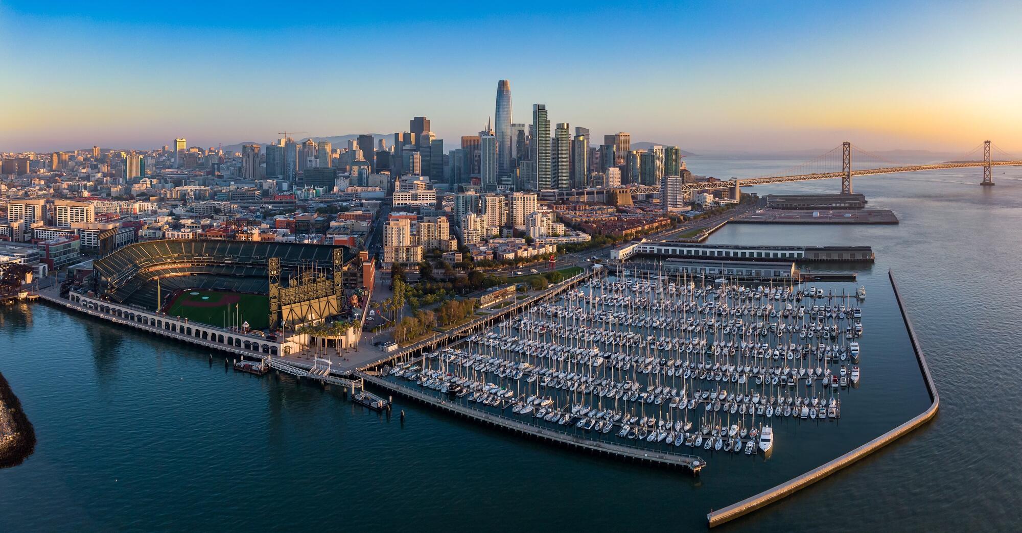 Eine weite Luftansicht zeigt die Liegeplätze von South Beach Harbor, das Baseballstadion und die Skyline dahinter.