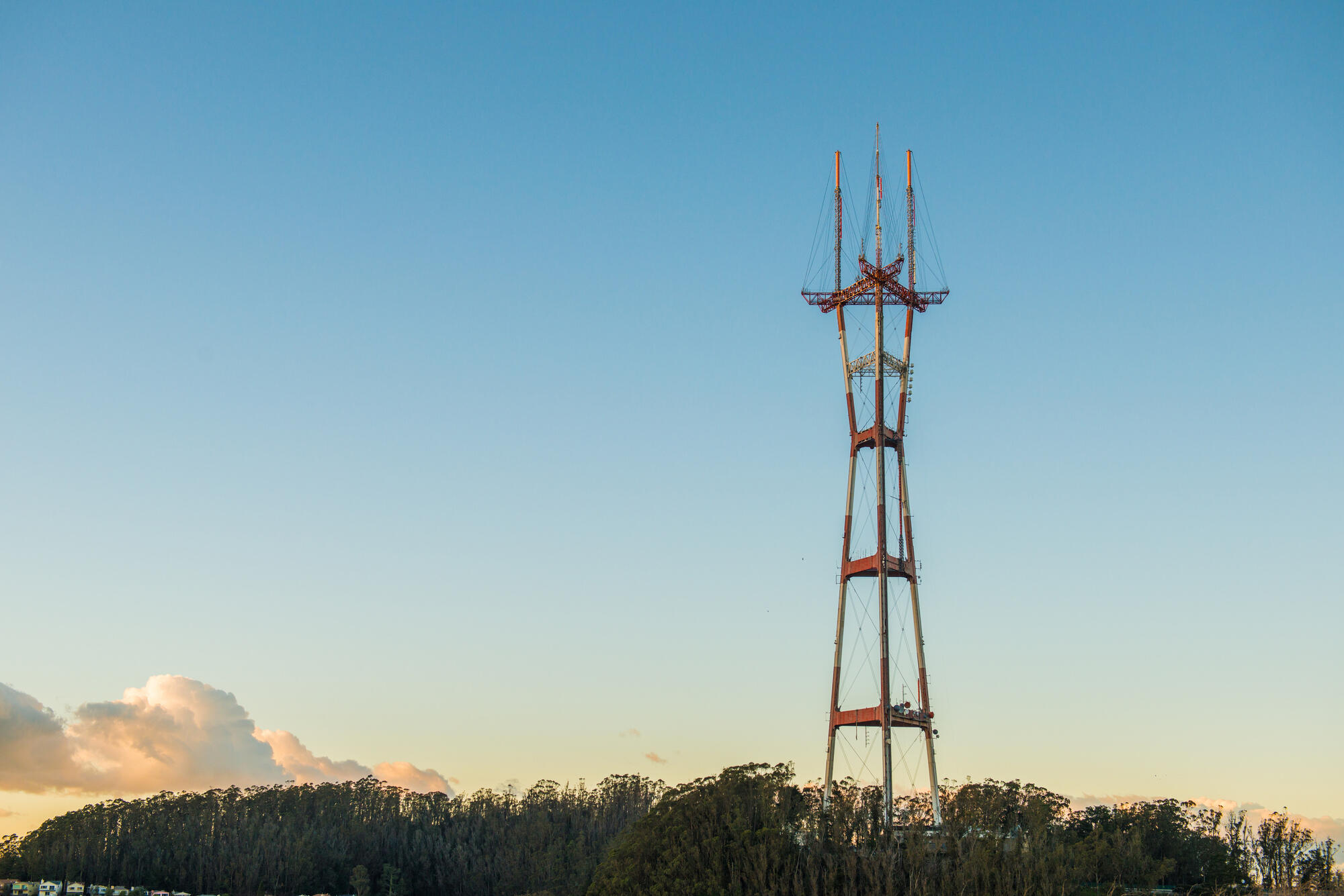 Die rot-weiße Stahlkonstruktion des Sutro Tower ragt über eine dunkle Baumlinie in den hellen Himmel.